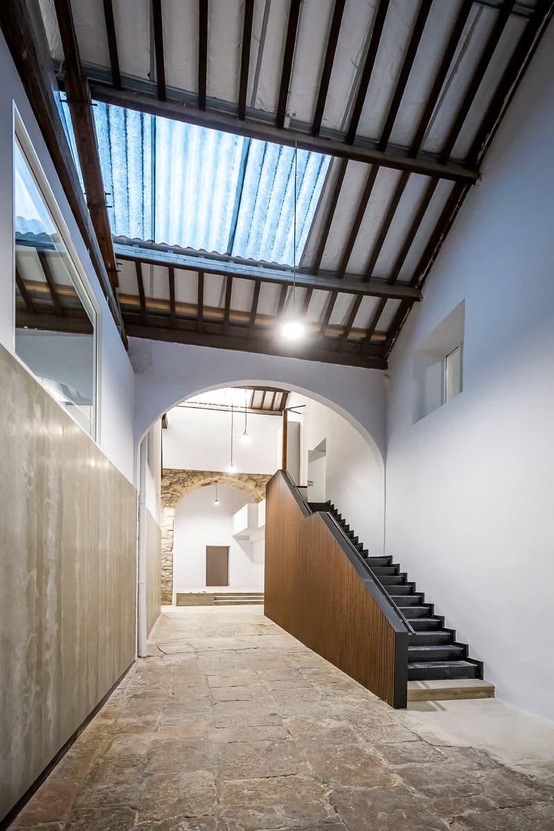 Interior del Centro de Formación Ocupacional en Avilés con arco de piedra, suelo antiguo y escalera moderna.
